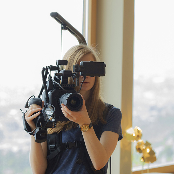Woman filmmaker with a Sony FS7 II cinema camera mounted on an Easyrig and controlled by the Caman multifunction camera grip